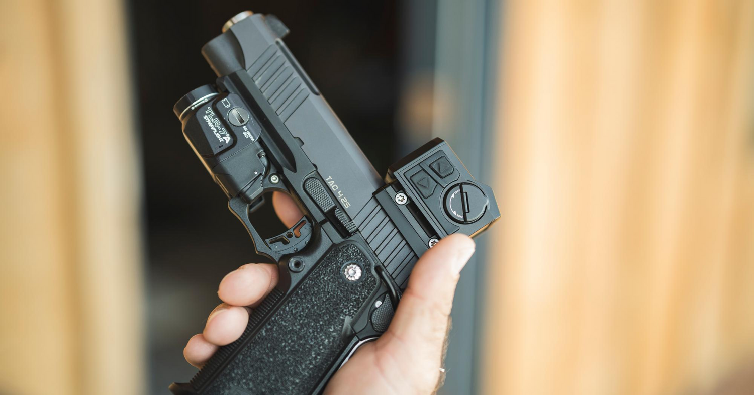 Close-up of a hand holding a black TAC 4.25 pistol with a Streamlight TLR-7A tactical light and a red dot sight mounted on top.