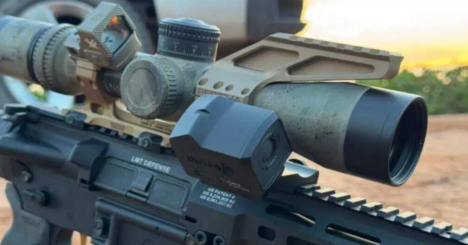 A close-up of a modern rifle featuring a sophisticated optics package, including a primary scope, an offset red dot sight, and a laser rangefinder module.