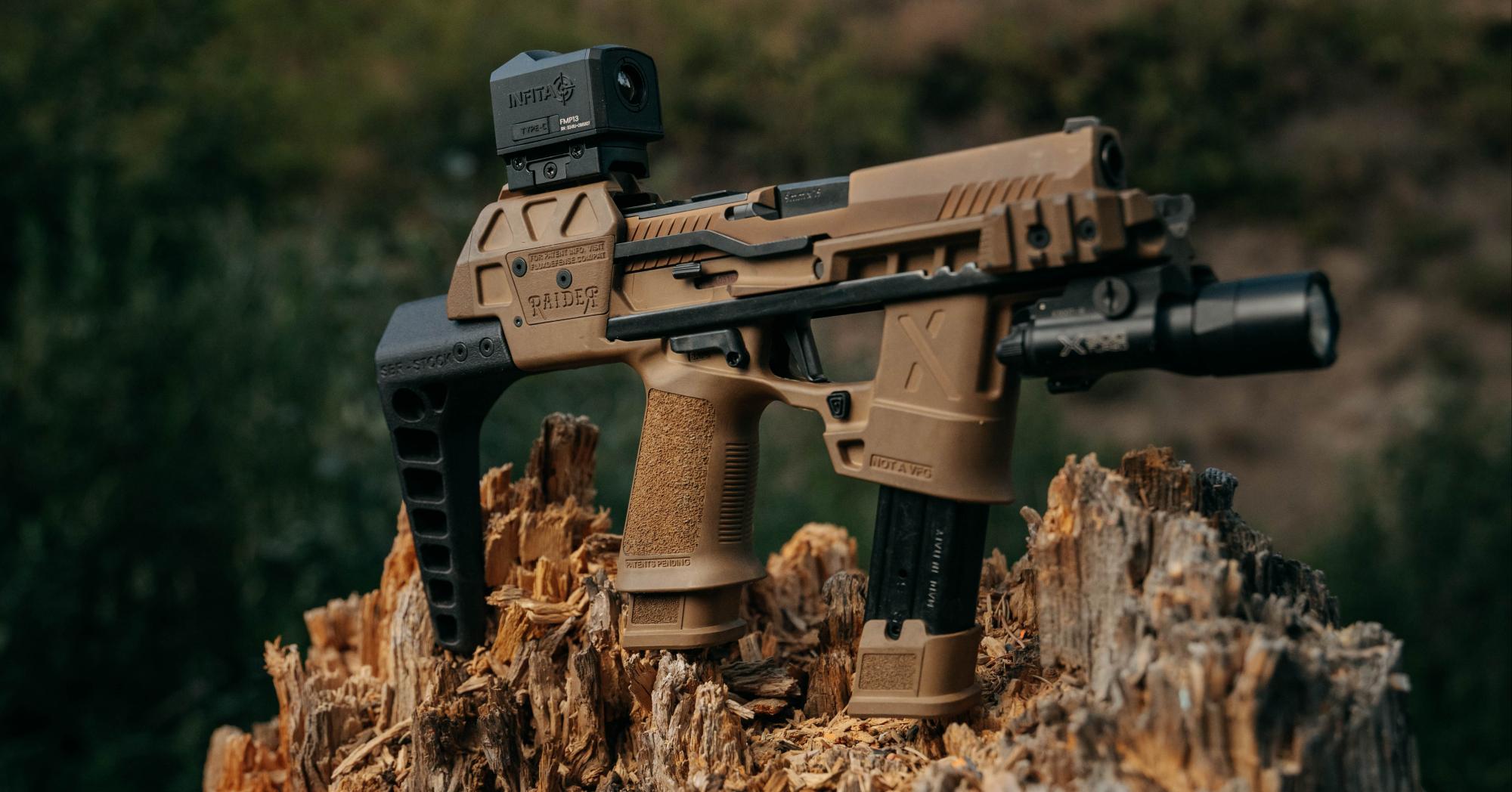 A tan Flux Raider chassis with an Infitac red dot sight and a weapon light, resting on a tree stump outdoors.