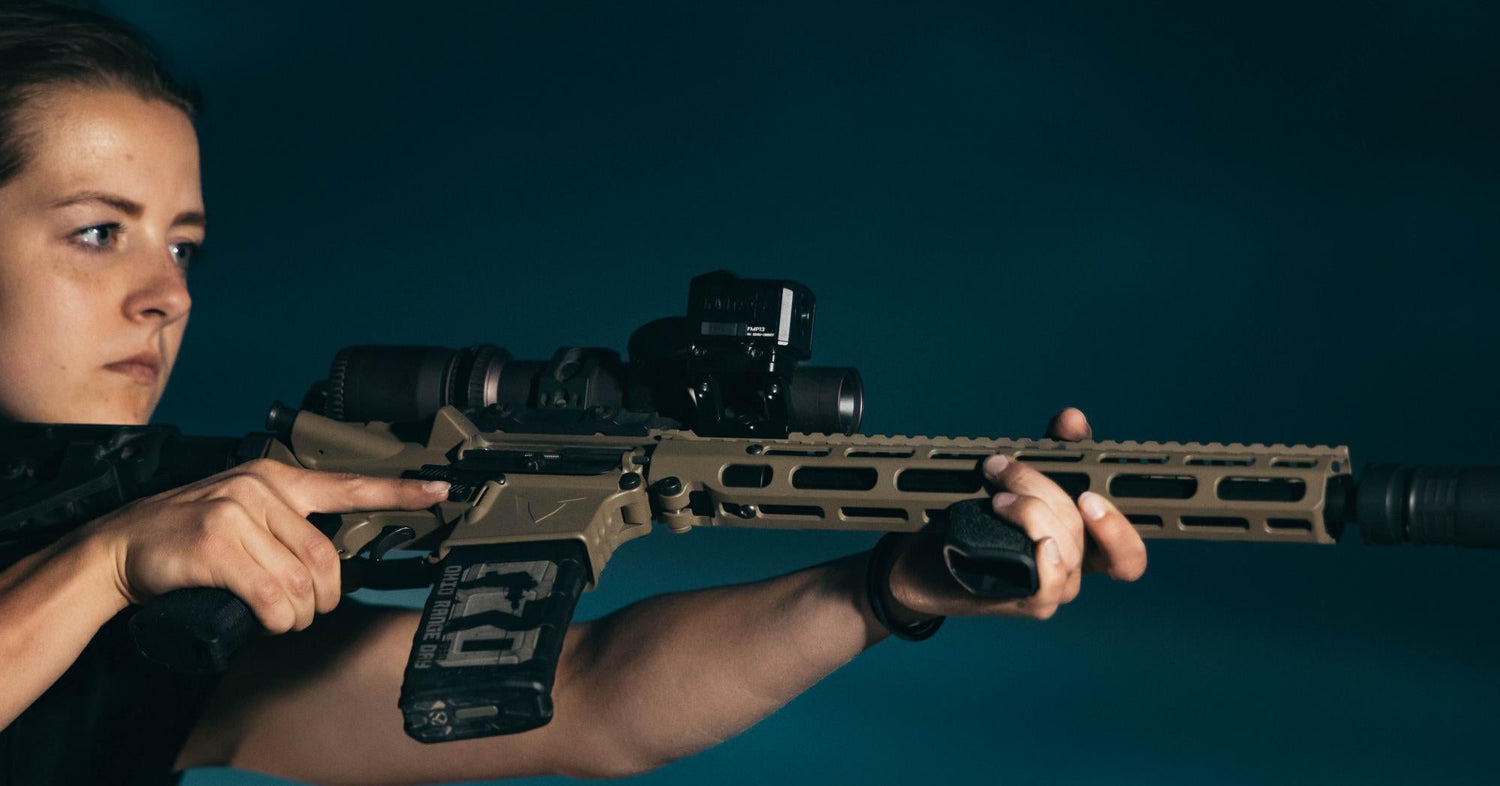 A woman with a focused expression holding a tan tactical rifle against a dark teal background.